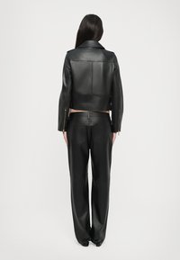 Sort lædercropped jakke med en glat tekstur og fremtrædende sømme, kombineret med højtaljede sorte læderbukser med baglommer.