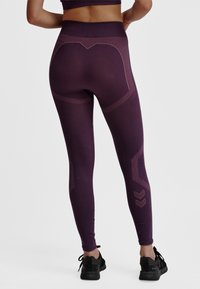 Paarse sportlegging met een hoge tailleband, voorzien van textuurelementen en een geometrisch ontwerp. Gecombineerd met zwarte sportschoenen.