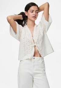 Bílá blůzka s krátkým rukávem z očkované látky, s uzavíráním na šňůrku vpředu a s vlnkovým lemem. Kombinováno s bílými kalhotami s vysokým pasem.