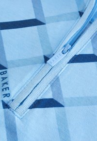 Tissu bleu clair avec des motifs géométriques bleu foncé et une tirette de fermeture éclair assortie gravée "BAKER" sur une poche zippée.