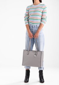 Borsa tote grigia con texture liscia e design strutturato, dotata di manici doppi e un piccolo charm, abbinata a un outfit casual.