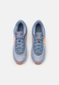 Lyseblå atletiske sneakers med struktureret mesh-overdel, orange detaljer og flade snørebånd. Har polstret krave og dæmpet gummisål.