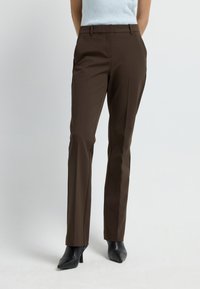 Bruine op maat gemaakte broek met een slim fit, voorzien van een soepele textuur, tailleband, zijzakken en een plooi aan de voorkant. Gecombineerd met zwarte hakken.
