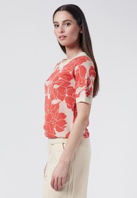 Knit short-sleeve sweater in coral with a floral pattern. Features a crew neck and light ribbed cuffs. Smooth texture, lightweight fabric.
