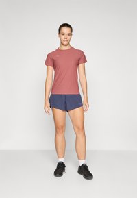 Conjunto de roupa desportiva composto por uma t-shirt de mangas curtas cor-de-rosa e calções escuros azuis. O material parece leve, com um design simples, combinado com sapatos pretos.