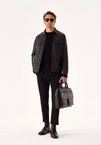 Chaqueta de cuero negra con dos bolsillos en el pecho, combinada con un suéter negro y pantalones. Bolsa de cuero negra con cremallera frontal. Botines de vestir negros.