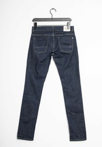 Jeans de mezclilla azul oscuro, corte ajustado, diseño de cinco bolsillos, con costuras en contraste. Etiqueta colgante visible en la parte trasera de la cintura. Textura suave.