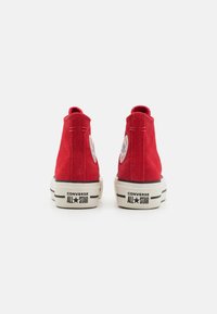 Czerwone zamszowe sneaker'y wysokie z okrągłymi łatkami z logo, białymi gumowymi podeszwami i czarnymi akcentami. Charakteryzują się płaskimi sznurówkami i wzmocnionym piętą.