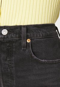 Vaqueros de mezclilla negra con una cintura alta, herrajes de cobre y una textura sutil. Presenta un bolsillo frontal y acentos de costura en las costuras.