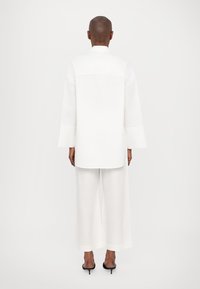 Top bianco largo e pantaloni a gamba larga, realizzati in tessuto leggero. Presentano maniche lunghe e una linea dritta all'orlo.