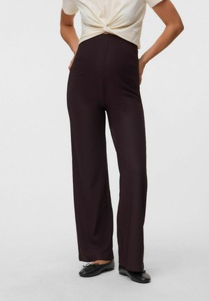 Personne portant un pantalon foncé taille haute à jambes larges avec des poches avant, associé à des ballerines noires et un haut crème noué.