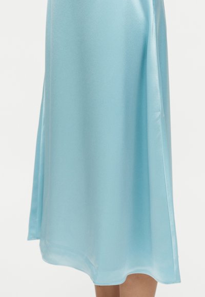 Φωτεινό μπλε σατέν μίντι φούστα με ίσια γραμμή και πλαϊνή σχισμή, φορεμένη στο μήκος μέχρι τη μέση της γάμπας.