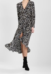 Svart klänning med vitt blommönster, långa ärmar, djup V-ringning, längd till mitt på vaden med en sidoklyv, lager på lager och flödande tyg.