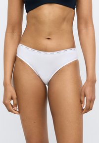 Hvide bomuldsbikinitrusser med en tynd elastisk linning med "GUESS"-logo i sort, som sikrer en tæt pasform og glat tekstur.