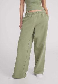 Pantalons de jogging larges et verts en coton doux, dotés d'une taille élastique et de poches latérales. Texture lisse avec des détails de couture minimalistes.