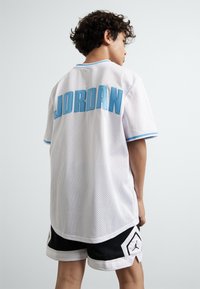 White mesh jersey with "JORDAN" in light blue on the back, paired with black basketball shorts featuring a white logo and accents.