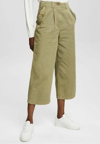 Khaki wide-leg pants made from cotton with a textured finish. Features pleats, two front pockets, and button accents. Worn with white sneakers.