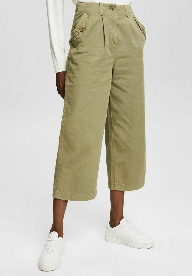 Khaki wide-leg pants made from cotton with a textured finish. Features pleats, two front pockets, and button accents. Worn with white sneakers.
