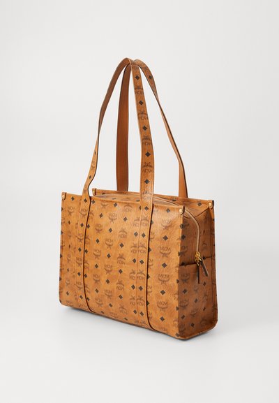 Tan leather tote bag with a patterned surface featuring repeating logos. It has two long handles and a zippered pocket on the side.