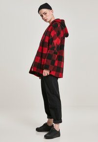 Rdeča in črna flisasta jopa s karirastim vzorcem, sproščenim krojem, z zadrgo spredaj in dvema stranskima žepoma, kombinirana s črnimi ožanimi hlačami in supergami.