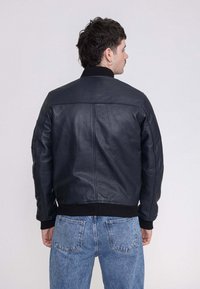 Zwarte leren bomberjack met een geribde kraag en manchetten, voorzien van een gladde textuur en een cropped snit, gecombineerd met lichtblauwe jeans.