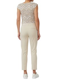 Pantalons beiges ajustés avec une texture lisse, associés à un haut à manches courtes à motifs présentant un motif en chevron dans des couleurs claires et foncées.