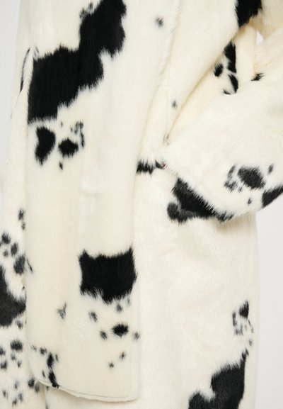 Abrigo de piel sintética en color crema con grandes patrones de vaca negra, que cuenta con una textura suave y bolsillos laterales para mayor funcionalidad.