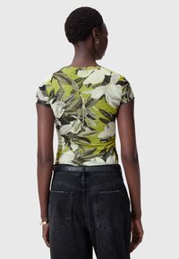 Blomstermønstret grønbluse med korte ærmer, tilpasset form og blød tekstur, parret med højtaljede sorte denimjeans med baglommer.