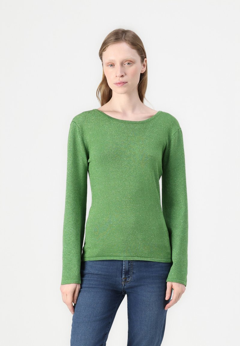 Grønn langermet genser med avslappet båtutringning og en glitrende tekstur. Kombinert med tettsittende blå jeans.