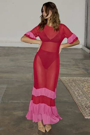 Red sheer dress with pink ruffled accents at sleeves and hem. Fitted bodice and flowing skirt, highlighting layered texture and contrast.