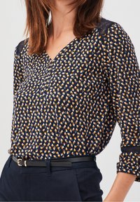 Navy blouse featuring a geometric pattern in yellow and white, with a V-neckline and three-quarter sleeves. Smooth fabric texture.