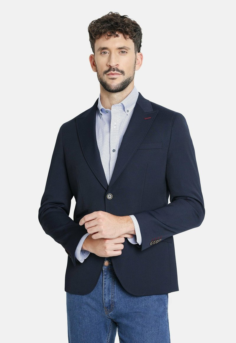 Blazer estructurado azul marino con solapas de muesca, cierre de botones y bolsillos, superpuesto a una camisa clara de rayas azules.