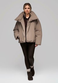 Beżowa kurtka puchowa z wysokim kołnierzem. Miękka, pikowana tekstura. W połączeniu z czarnymi legginsami i ciemnymi botkami, prezentuje nowoczesny wygląd.