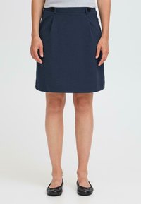 Gonna blu navy fino al ginocchio con frontale piatto, due tasche laterali e decorazioni a bottoni sulla vita. Indossata con scarpe flat nere.
