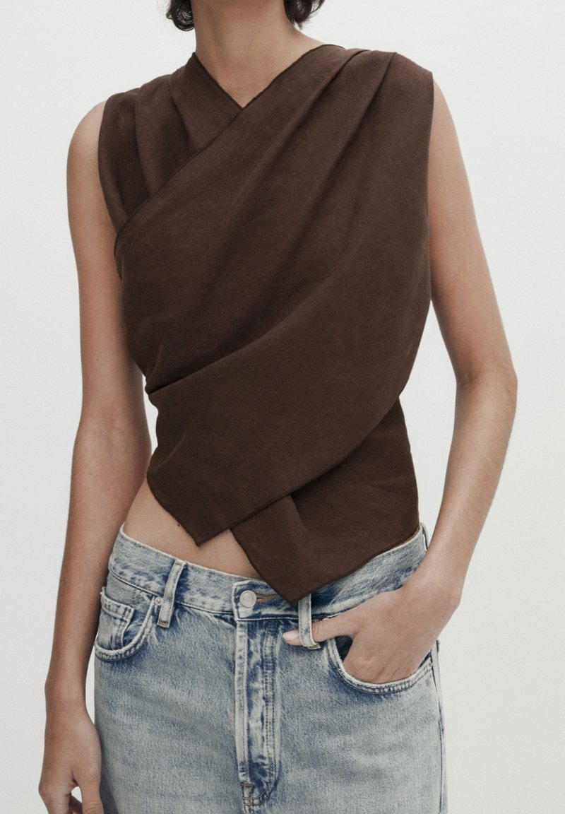 Haut marron sans manches avec un design plié, en tissu léger. Associé à un jean clair déchiré taille haute.