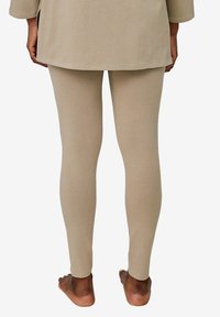 Beige Leggings aus weichem, dehnbarem Material, die eng an den Beinen anliegen, mit einer glatten, matten Textur.