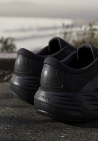 Pair of black athletic shoes with cushioned soles resting on a rough outdoor surface near blurred natural background.