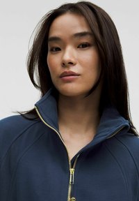 Navy zip-up jacket with high collar, gold zipper, and textured fabric. Features a fitted design with subtle stitching details.