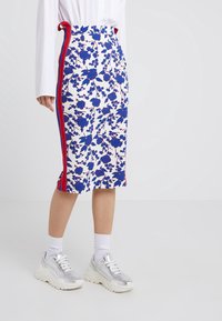 Květinová tužková sukně v bílé barvě se modrými a červenými akcenty, s bočními pruhy. Nošena s stříbrnými teniskami a bílými ponožkami.