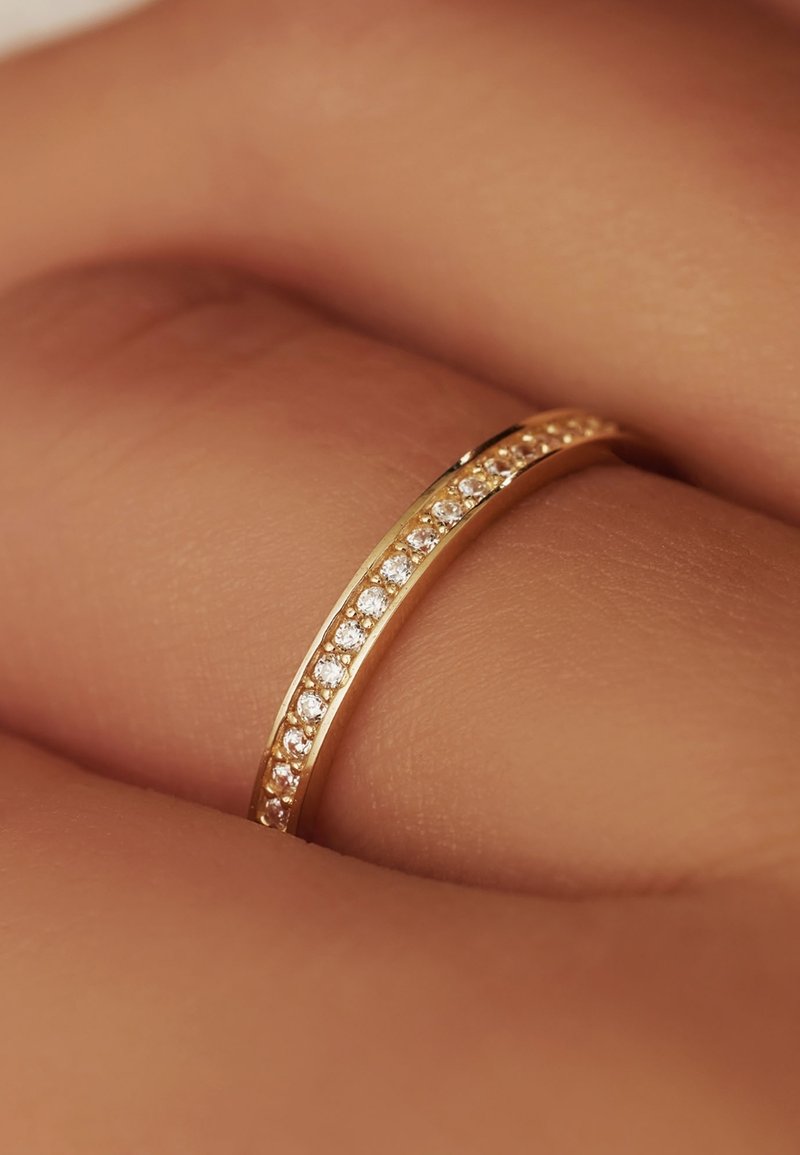 Goldring mit einem schlanken Band, das entlang der oberen Kante mit mehreren kleinen, klaren Edelsteinen besetzt ist, auf einer Hand ruhend.