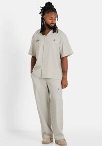 Ensemble à rayures comprenant une chemise à manches courtes et un pantalon ample en beige avec des rayures foncées et des détails brodés subtils.