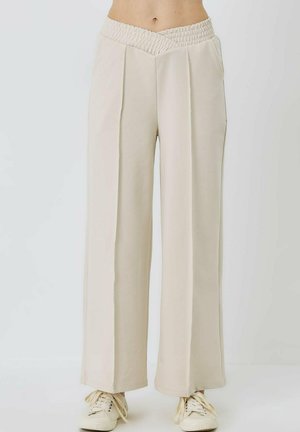Weite Hosen aus hellbeigem Stoff mit einem gesmokten Bund und seitlichen Taschen; glatte Textur mit gefältelten Designelementen.