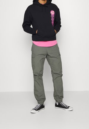 Felpa nera con stampa grafica, maglietta interna rosa, pantaloni cargo verdi oliva e sneakers alte nere con dettagli bianchi. Outfit casual.