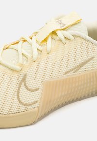 Tenis de plasă galben deschis, cu o talpă din cauciuc texturat, design subțire cu șireturi și o talpă intermediară parțial transparentă distinctivă.