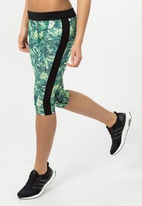 Leggings capri de patrón tropical en verde y negro, con una franja lateral negra. Combinados con zapatillas deportivas negras.