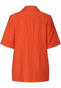 Lyhythihainen, kauluksellinen paita kirkkaan oranssina, valmistettu teksturoidusta kankaasta ja löysästä istuvuudesta. Takana on pystysaumadetaljointi.