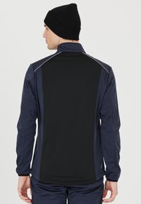 Marineblauwe sportjack met zwarte panelen, hoge kraag en ritssluiting. Bevat reflecterende accenten op de schouders en een gladde textuur.