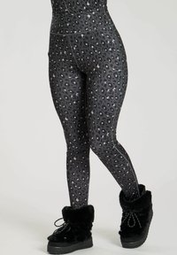 High-waisted black leggings with gray leopard print, worn with black fur-lined winter boots with laces against a plain background.