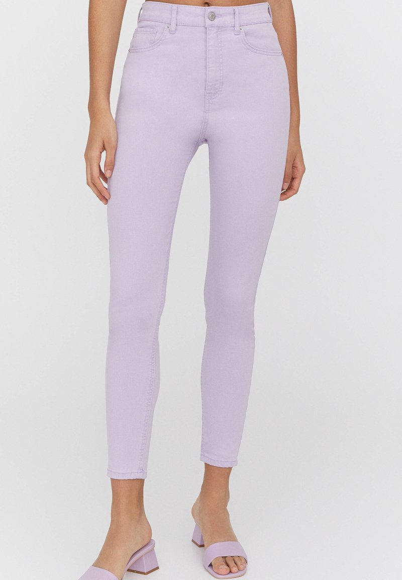 Jean skinny violet clair à taille haute, avec des détails de couture subtils et cinq poches, associés à des sandales à talons blocs lilas.