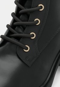 Gros plan d'une botte en cuir noir avec des lacets ronds noirs passés dans des œillets métalliques dorés.
